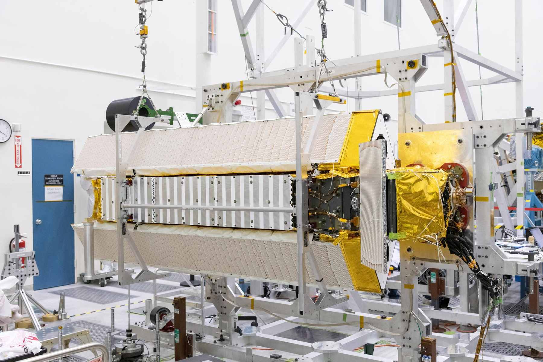 A satellite instrument payload on an assembly stand in a white clean room, wrapped in gold thermal blanket.